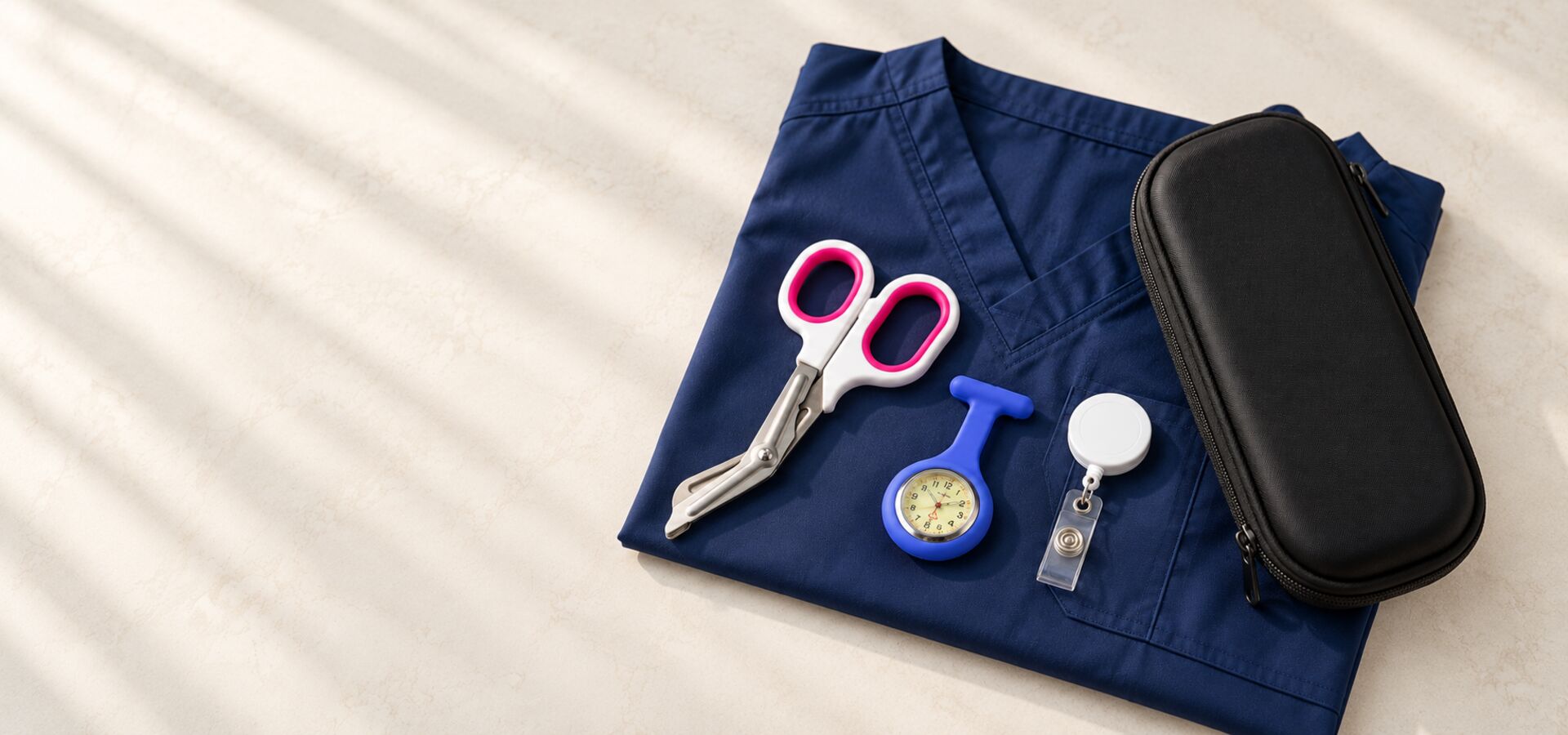Blue nurse fob watch, pink trauma shears, ID reel and black case on navy scrubs.
