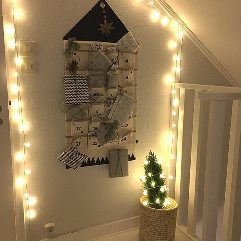 Black fabric advent calendar hanging in a hallway with fairy lights