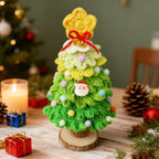 Light green crochet Christmas tree desk decoration beside candles and gift boxes